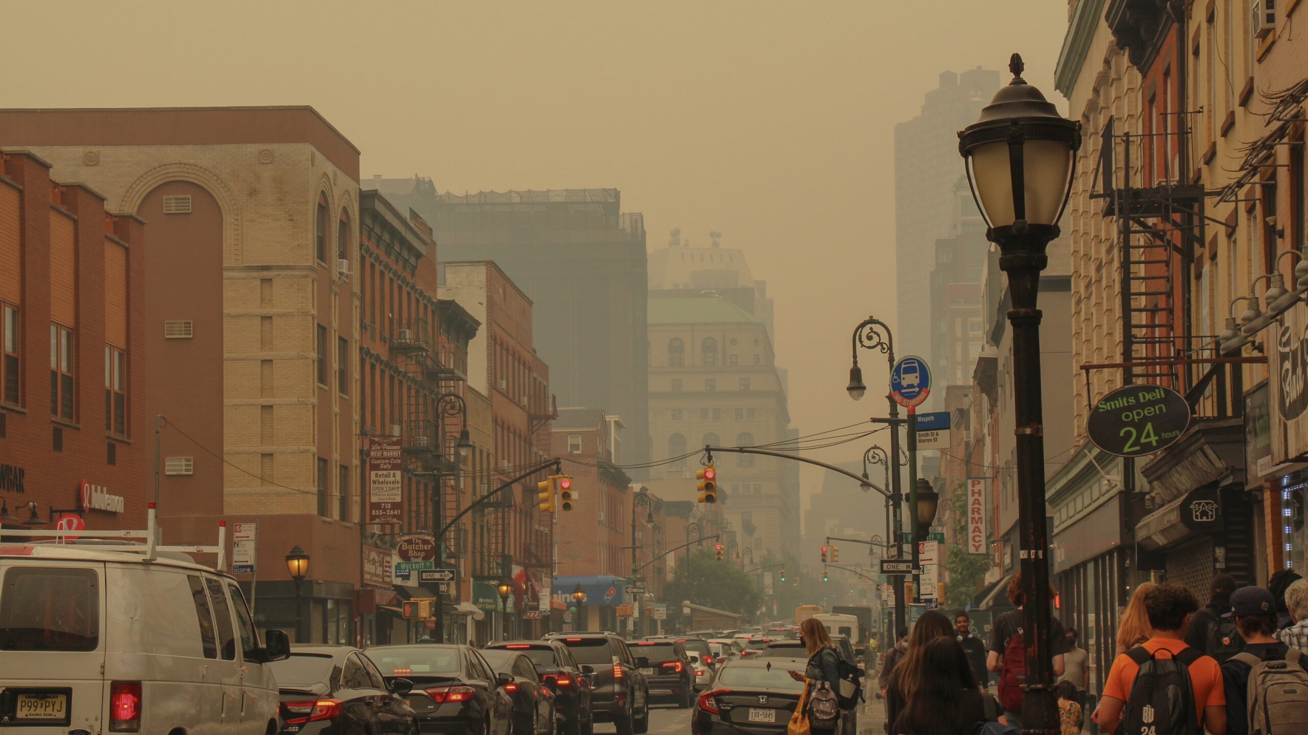 A busy street in New York City filled with cars. An orange gloomy hue billows the air and prohibits a clear view from buildings far away.