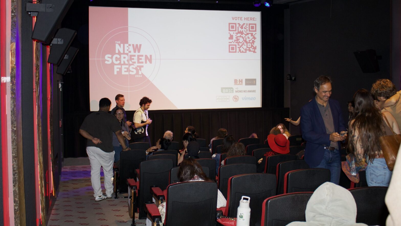 Movie theater with audience and a screen that says "New Screen Fest" with barcode