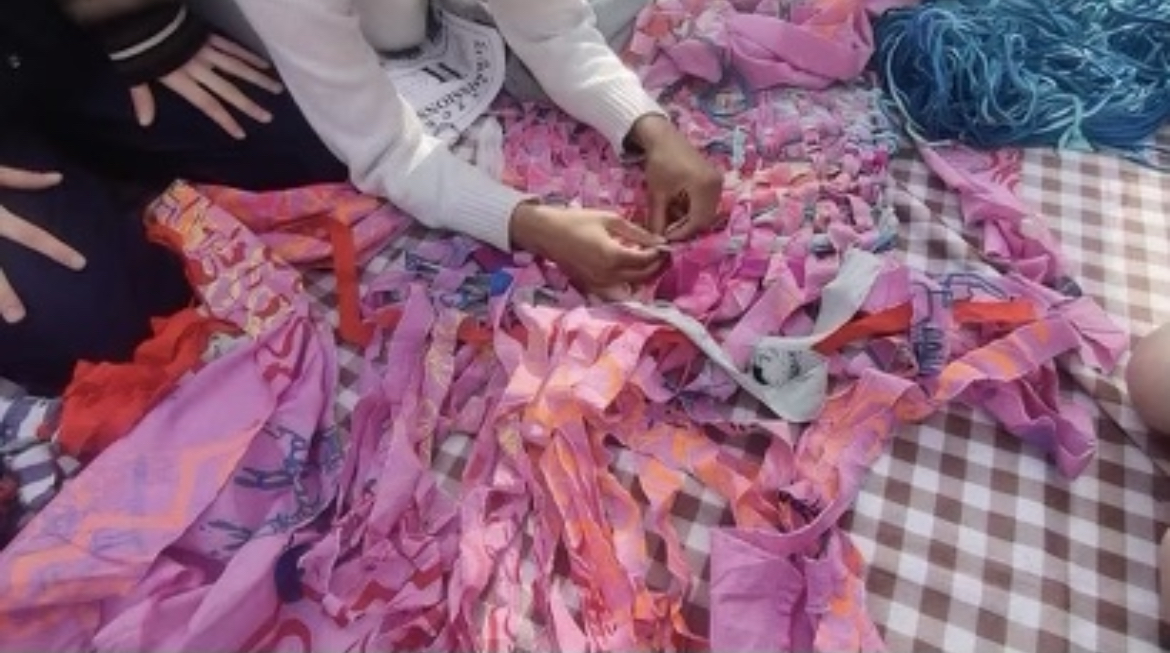 Photo of hands working on a multi-colored, mostly pink weaved piece.