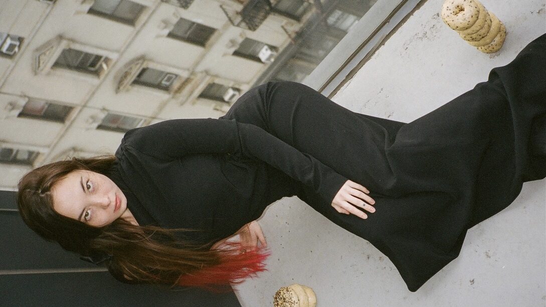 Sakura Smith in a black dress lying next to piles of bagels.