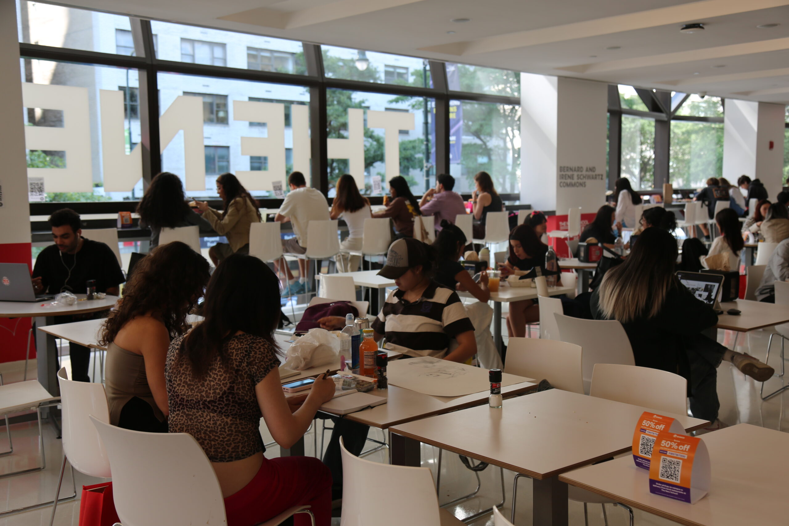 Students gathered in dining hall sitting at white tables and on white bar stool chairs