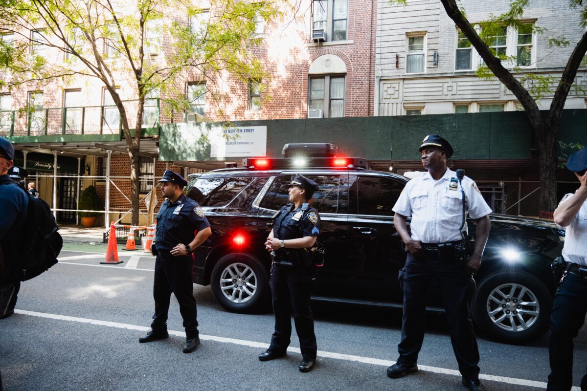 Four NYPD officers stand across from the Eugene Lang College building, with a police car behind them.