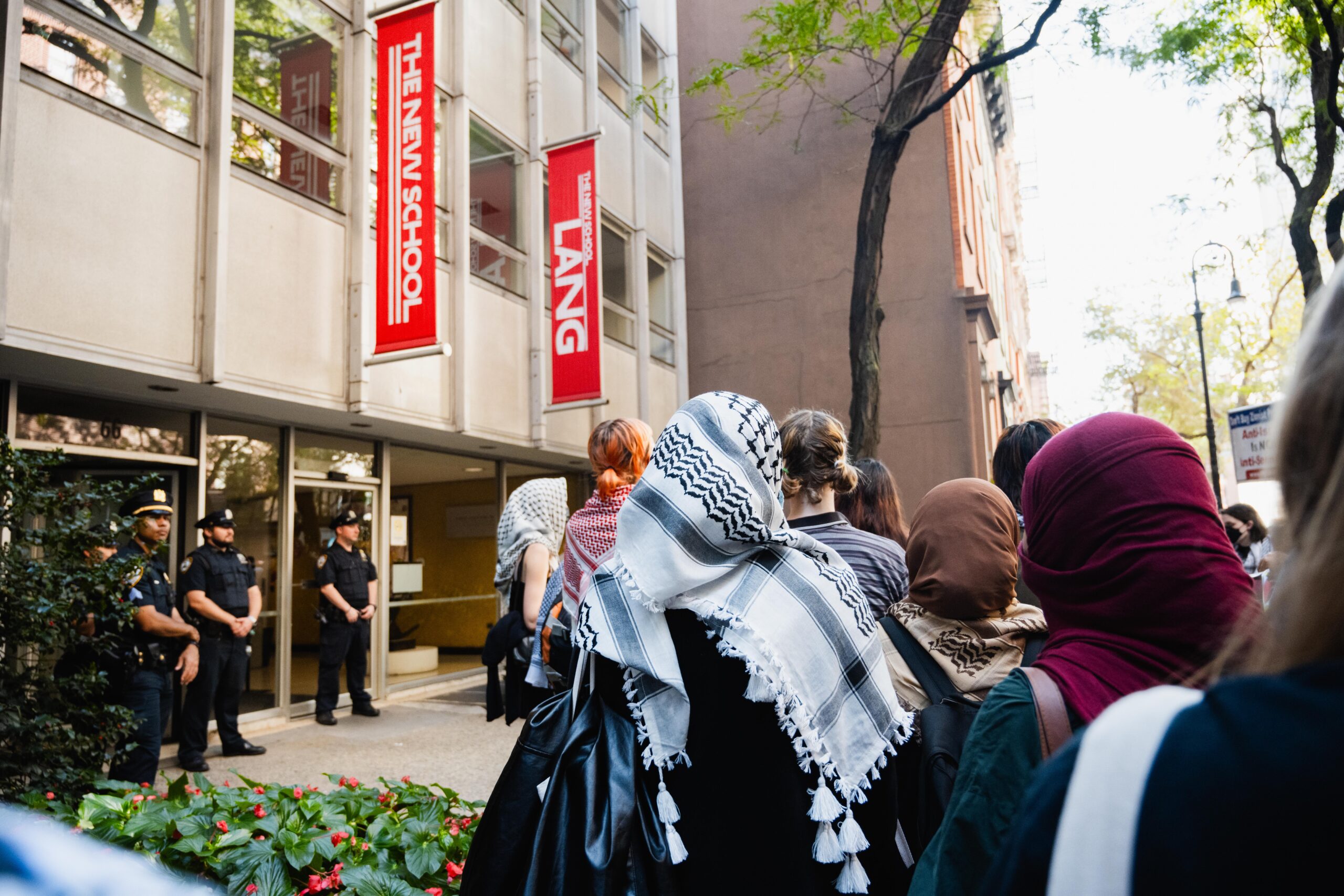 Student demonstrators gather outside of Lang while three NYPD officers stand in front of the entrance.