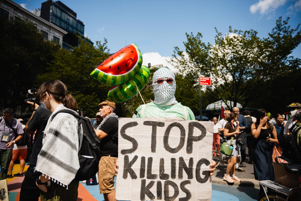 Protesters standing in front of a crowd holding a sign that reads "stop killing kids"