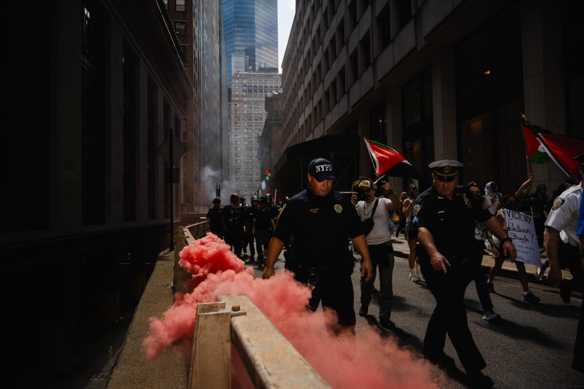 police officers leading a crowd of protesters with red smoke following them