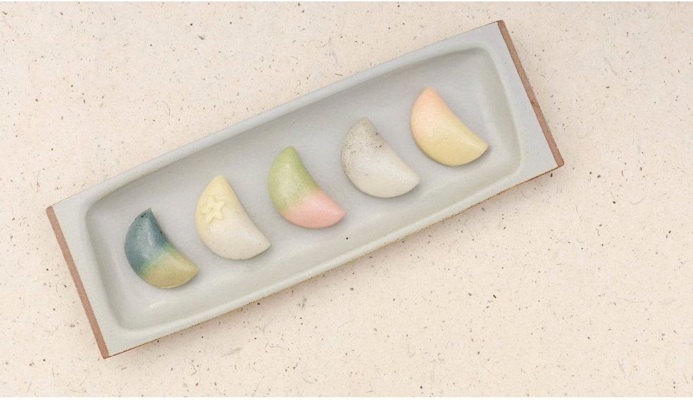 5 multicolored rice cakes in the shape of semi-circles on a grey rectangular plate. 