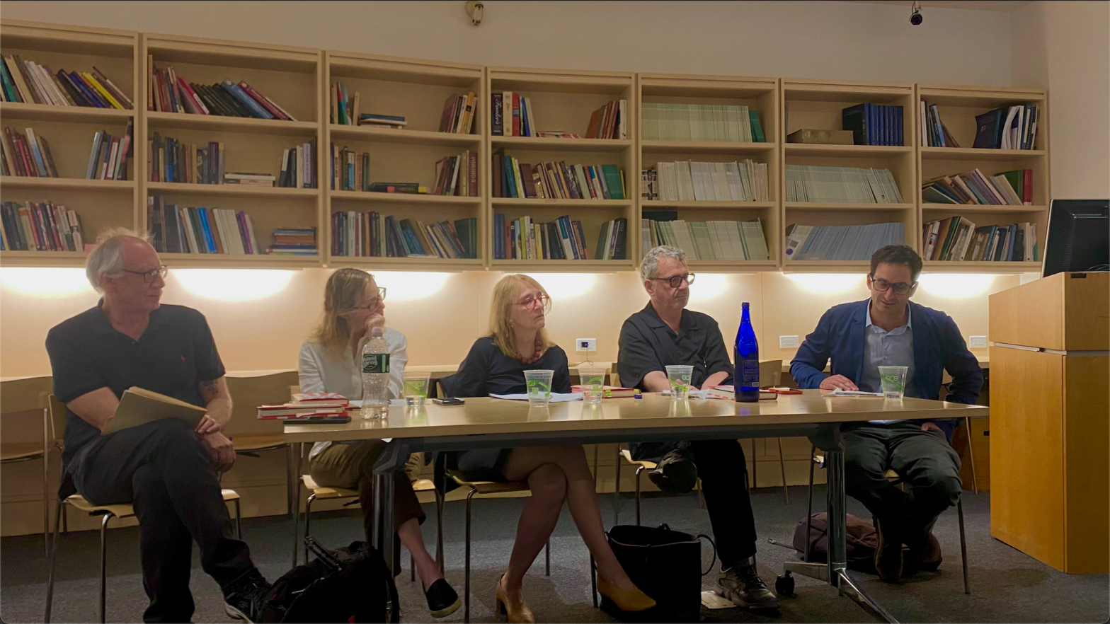 Five people sitting at a conference style table with cups and books in front of them.