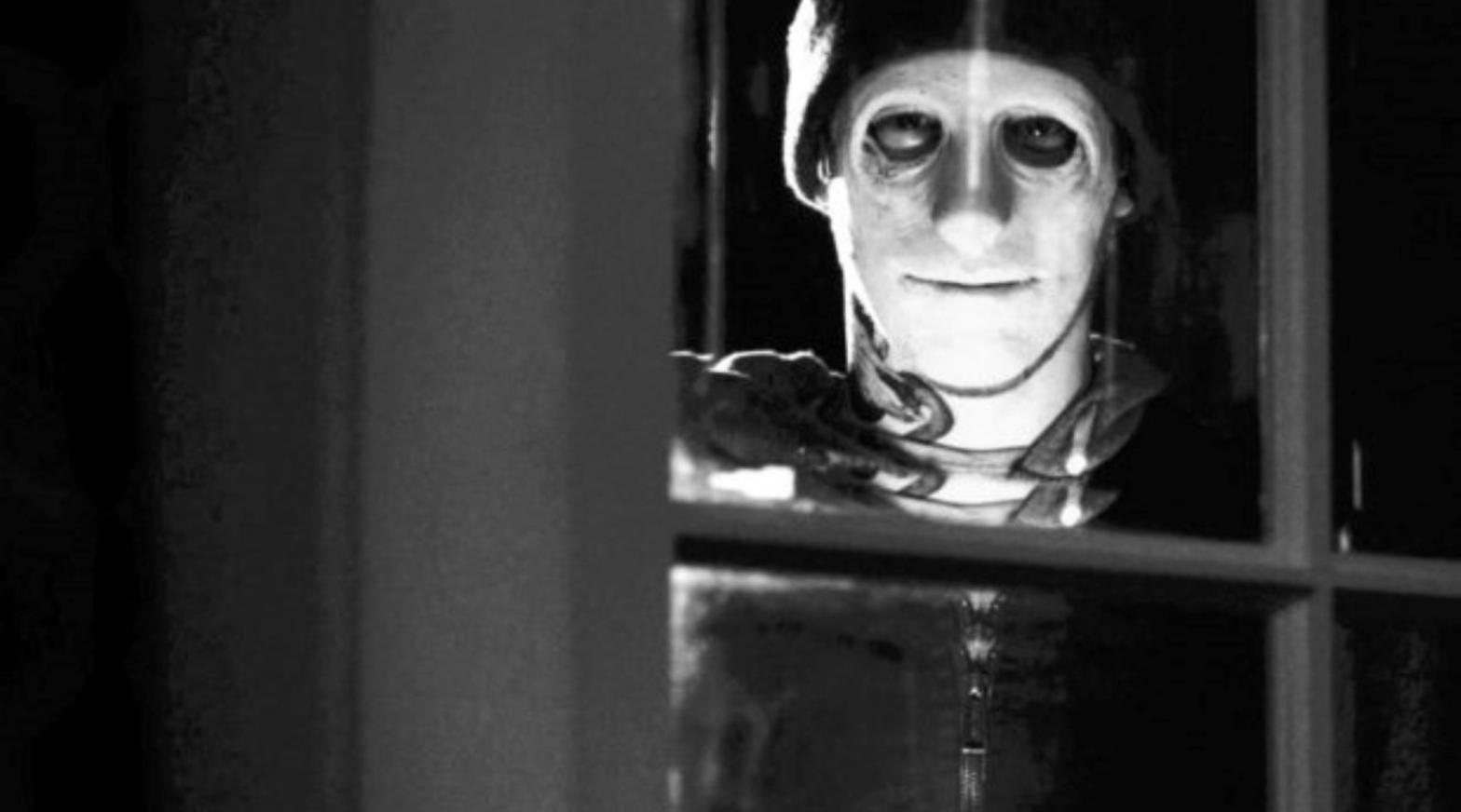 A photo of the masked killer from the film Hush, standing outside the house, looking in through the window.