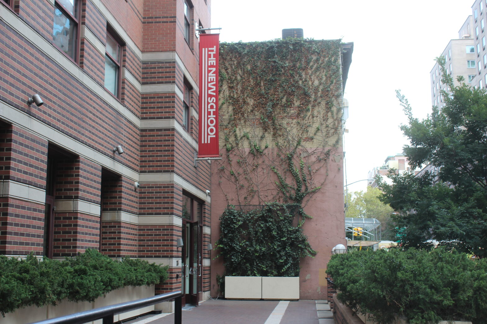 A photo of Loeb Residence Hall from the right side. A red New School banner hangs above the entrance of the building. In front of the entrance is a small patio with an accessible ramp leading up to it.