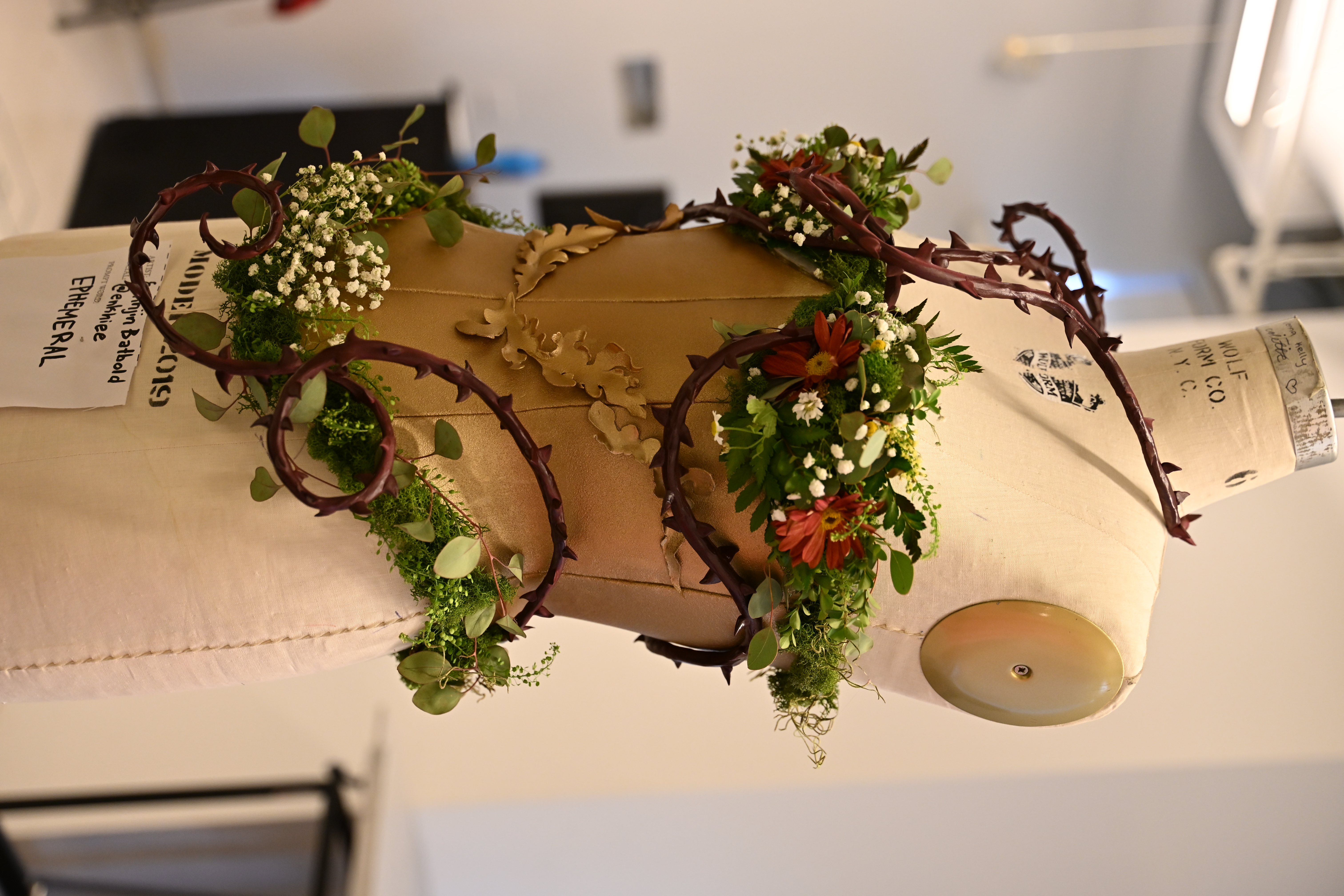 Corset bodice on a mannequin, wrapped thorns and greenery around it, flowers and eucalyptus. 