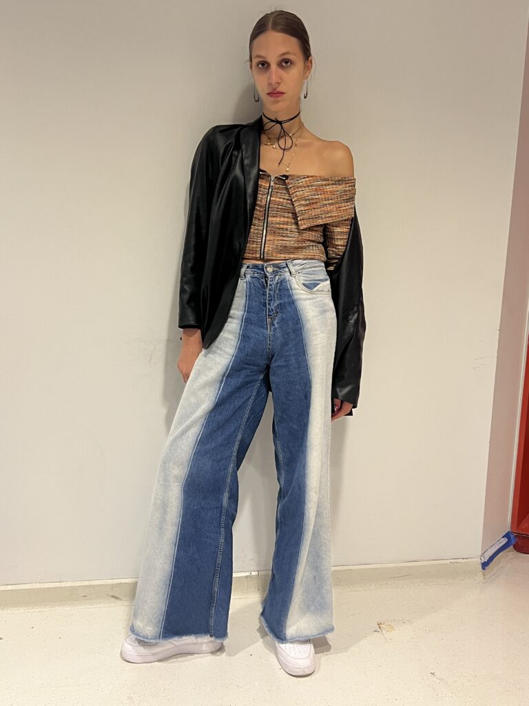 Student wears white sneakers, two-toned jeans, a multi-colored striped top, a black leather jacket, teardrop-shaped earrings, and layered necklaces along with a black ribbon choker. 