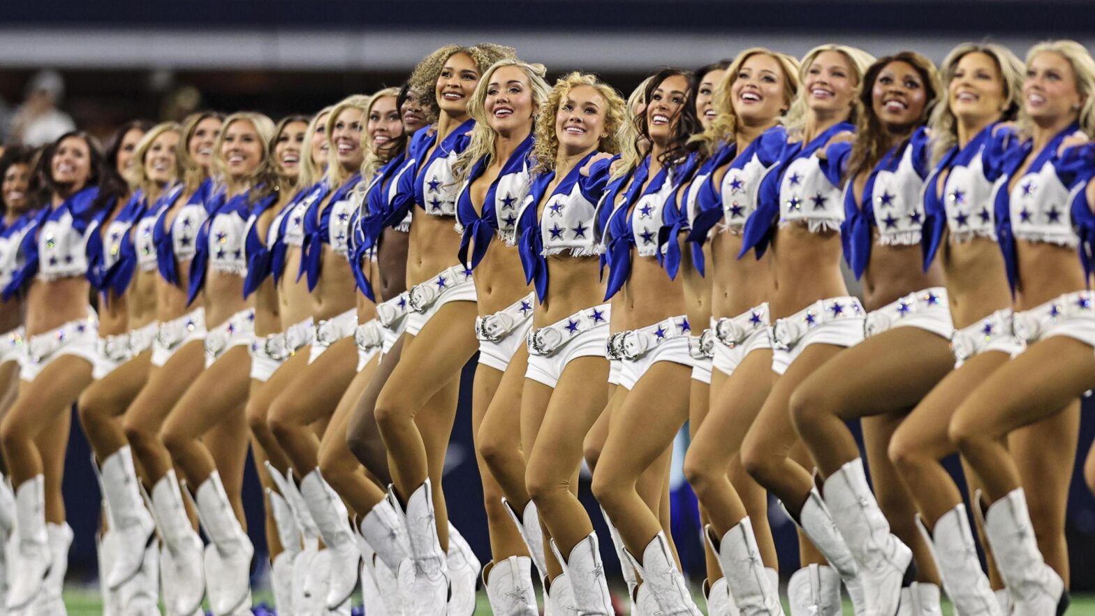 A group of cheerleaders in blue and white outfits featuring star emblems, standing in a line