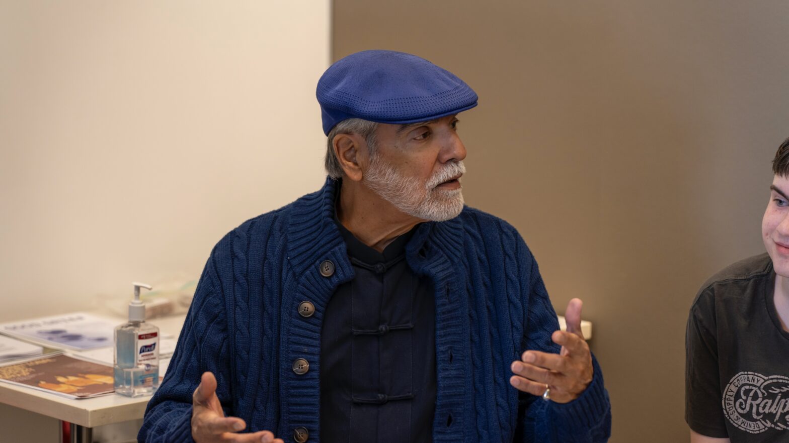 Man in a blue hat and sweater speaking in an expressive way