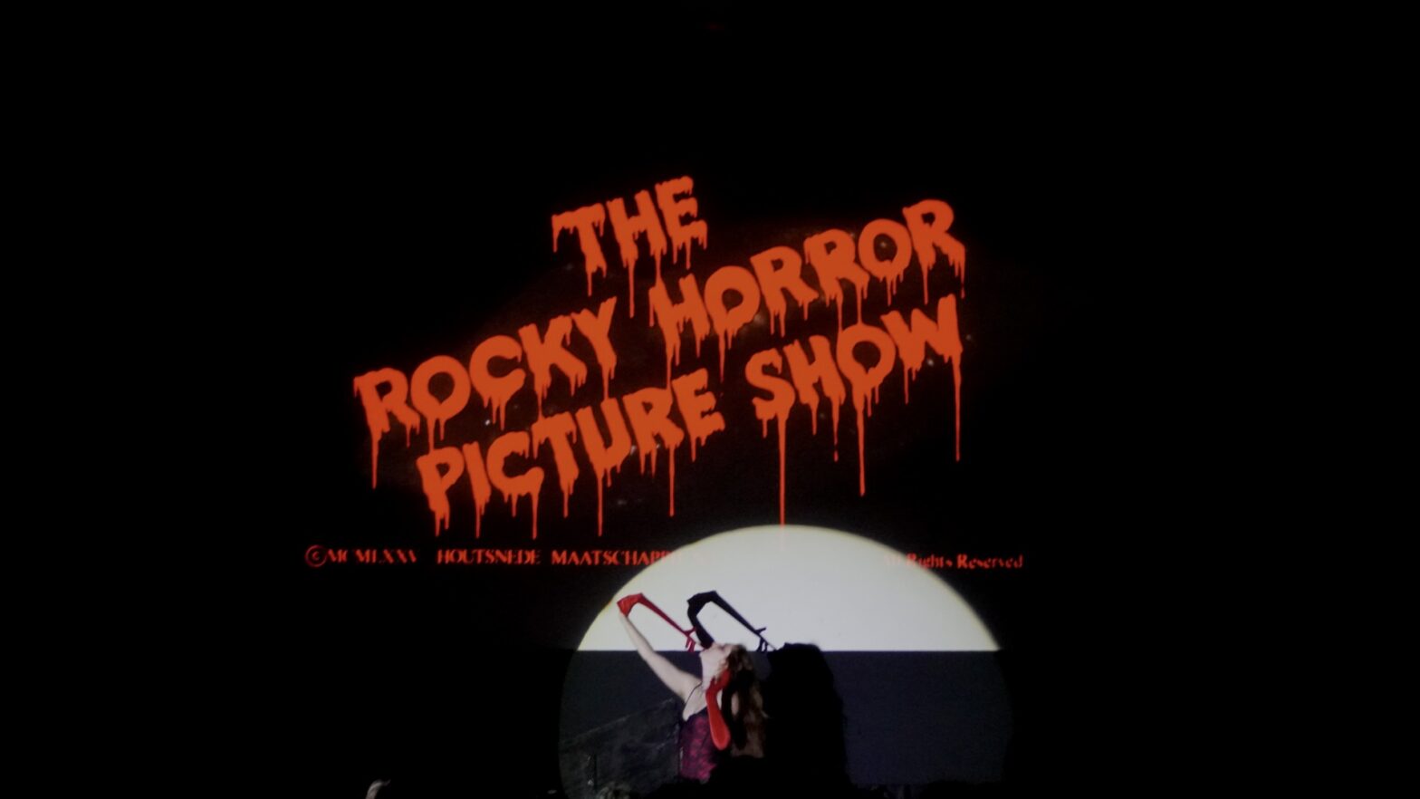 Dripping blood-red words that say The Rocky Horror Picture Show with a woman pulling a red glove off her hand with her teeth.