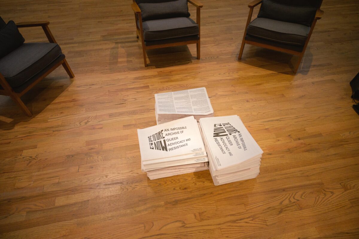 Three stacks of newspapers on a hardwood floor, in the middle of several chairs.