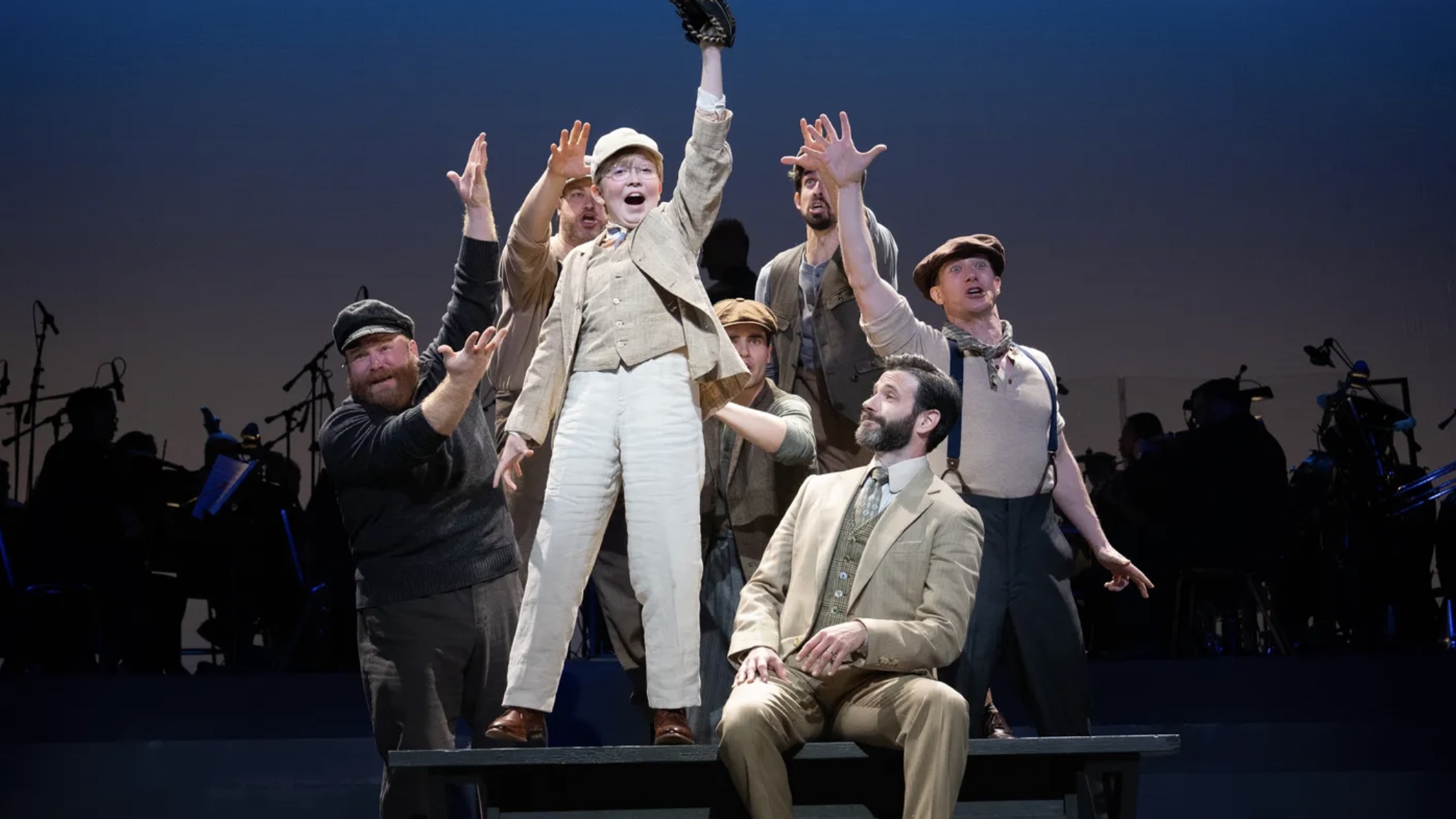 A small boy in white raises his fist in excitement while a group of older men around him point to him and look at him.