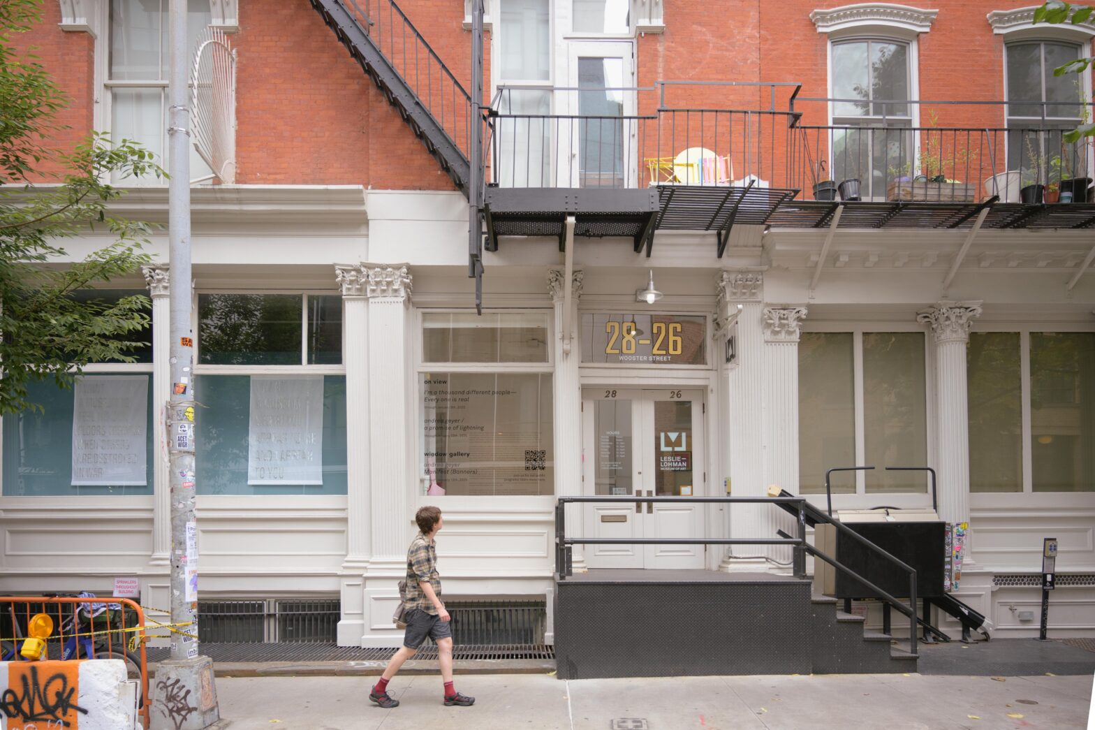 Person walking past a white building with columns, large windows, and the numbers 28-26 on the front window.