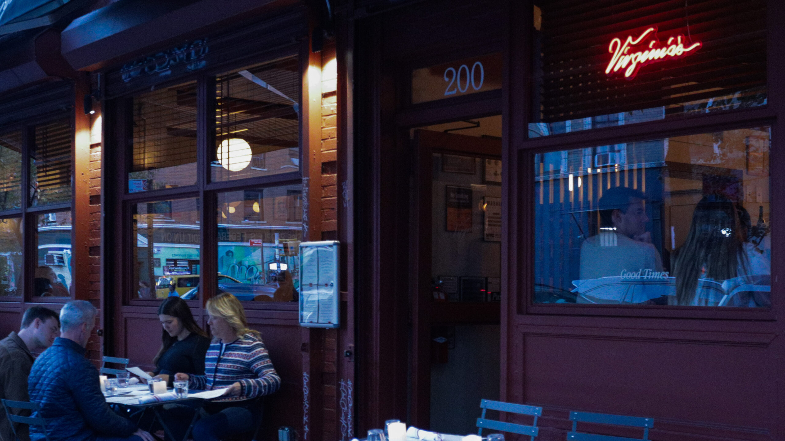 A group of four dining outside a restaurant, with a neon sign above the restaurant's window reading, “Virginia’s” in red cursive font