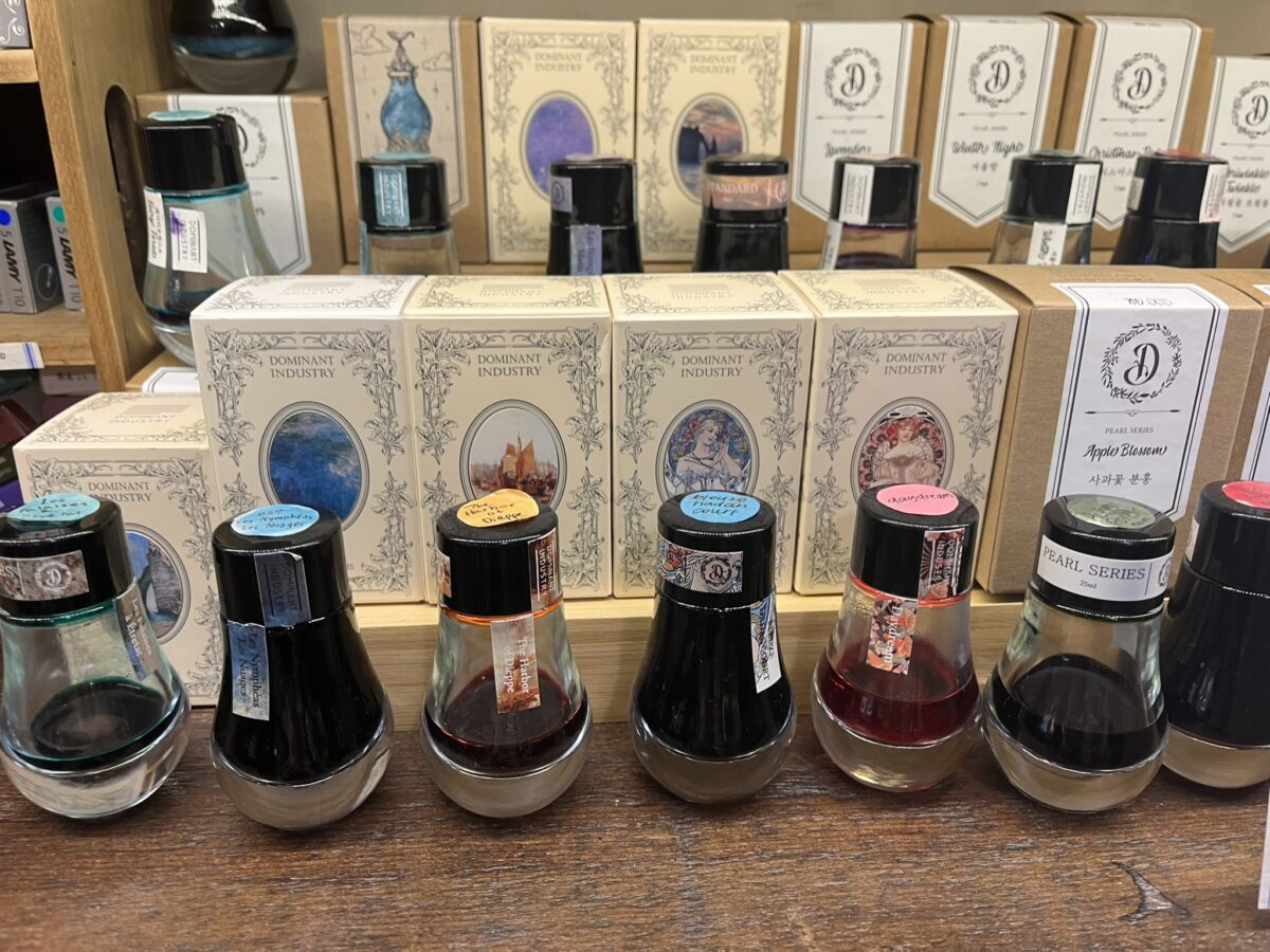 Bottles of differently colored inks by Dominant Industry with box packaging behind the bottles.