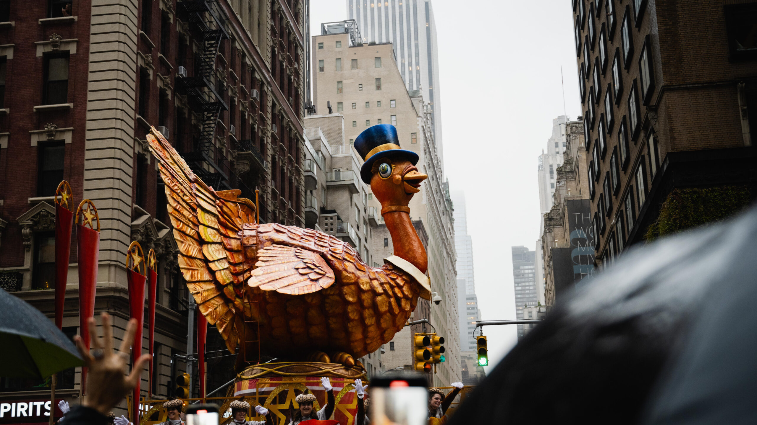 Large turkey float wearing a top hat. In the background, gray and brick buildings in the rain.