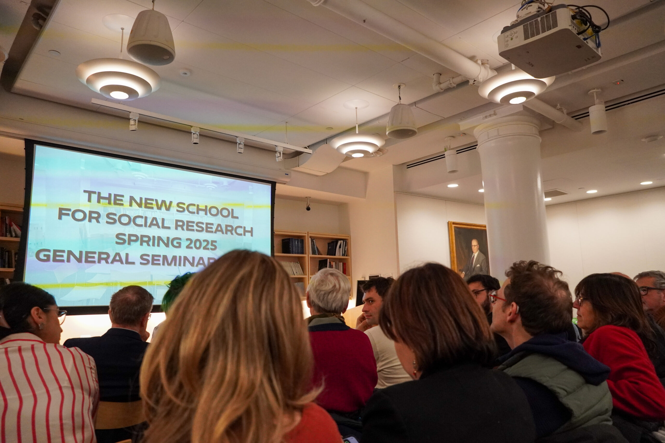 Projector screen at the front of the room with text “The New School for Social Research Spring 2025 General Seminar”, audience seated behind a screen