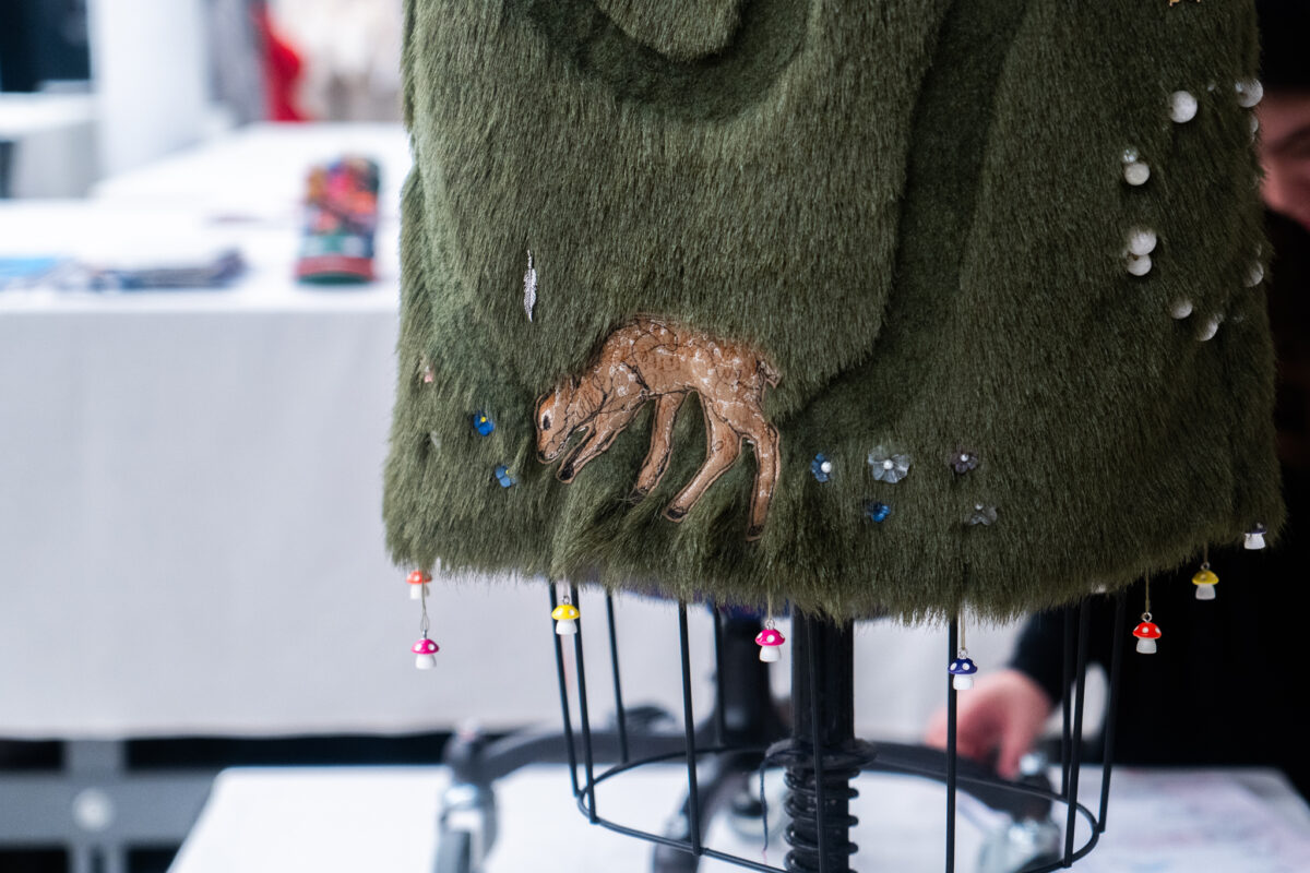 Closeup of grass-like fabric with tiny mushroom and flower details, felt deer cutout in center.