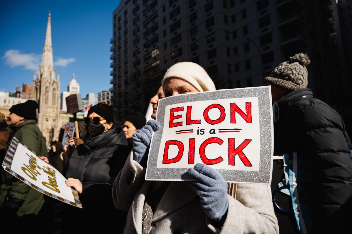 A protester holds a sign that reads, “Elon is a Dick”.