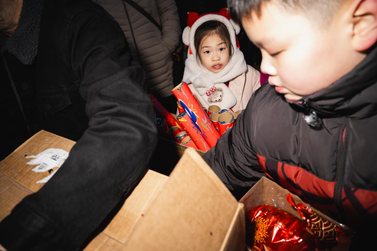 A young parade attendee dressed in red and white stares past boxes of confetti cannons. 