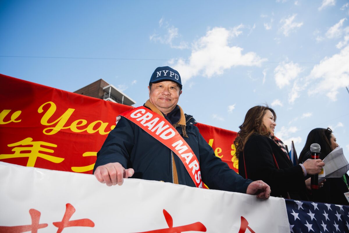 Parade Grand Marshal Peter Tu, executive director of the Flushing Chinese Business Association, wears a red “Grand Marshal” sash and New York Police Department hat against a red banner.