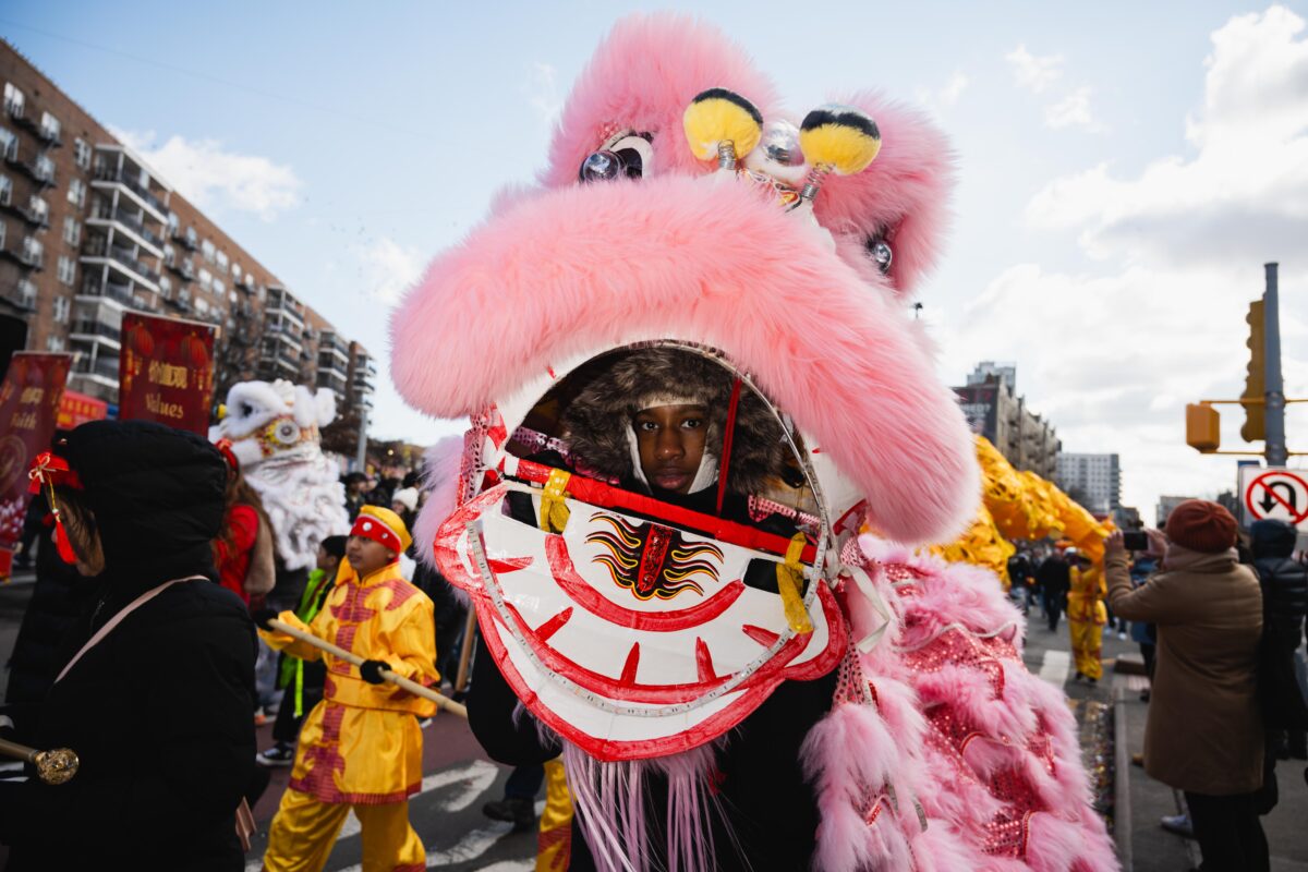 A performer operates a pink dragon puppet, peering out of the head.