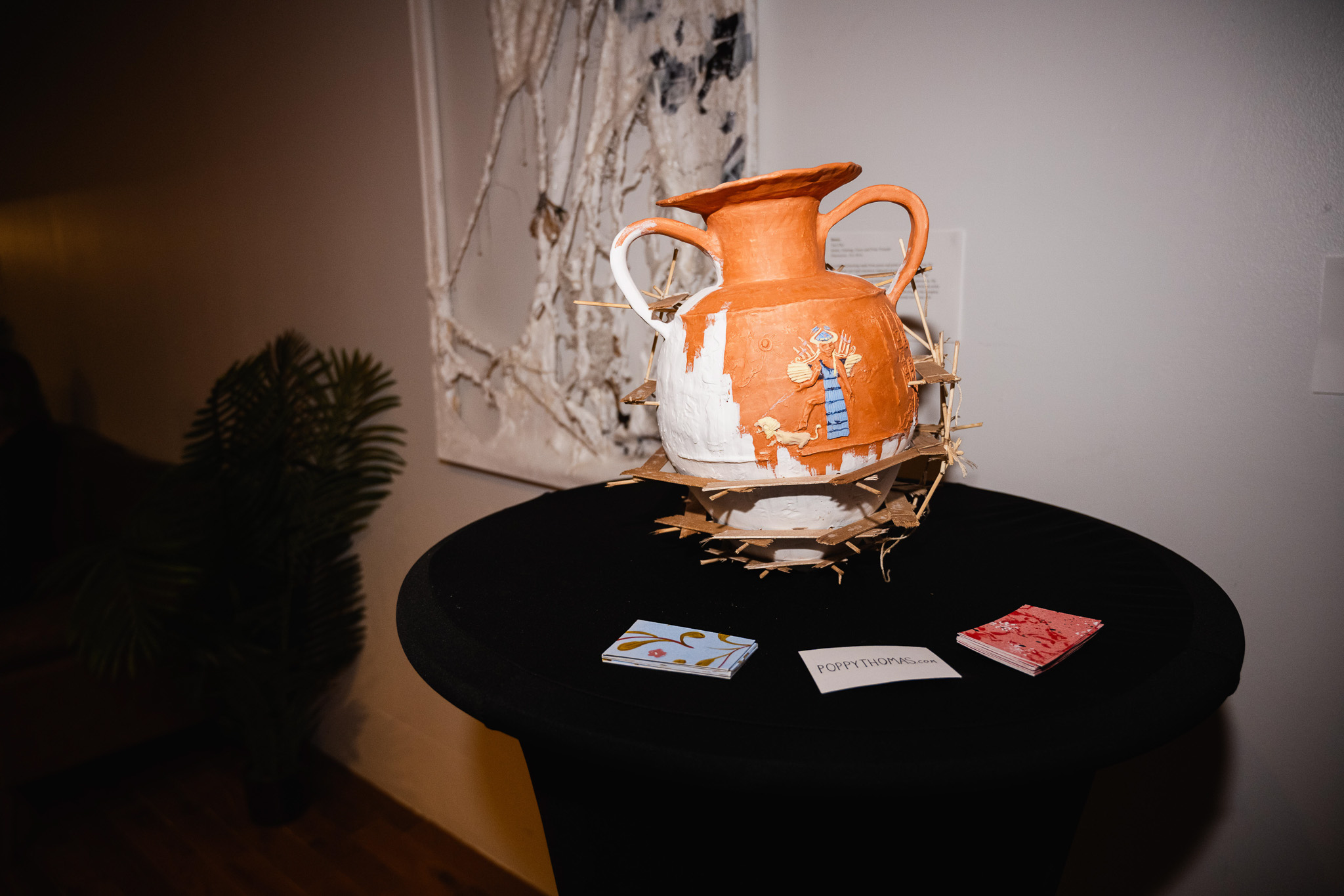 An intricate orange and white vase is atop a black table shone cast in the light against dark shadows.